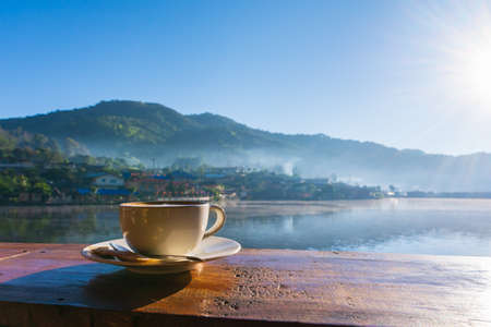 Hot coffee latte in coffee cup with beautiful view in morning sunrise light at Ban Rak Thai, Mae Hong Son, Thailand.の写真素材