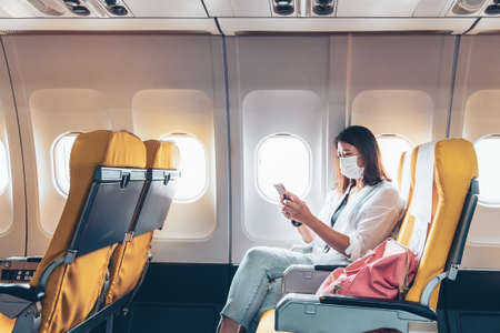 Woman traveler passenger sitting at airplane seat using smartphone onboard in new normalの写真素材