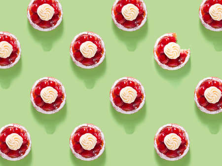 Pattern with many Cakes with strawberries, decorated with cream and powdered sugar on a green background, one bitten tartlet,の写真素材