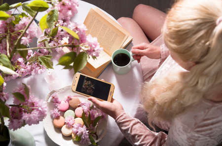 young blonde in pink dress drinking coffee and filming a video for her blog, top view from an angle,