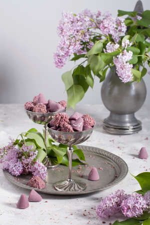 Belgian sweets cuberdon and pralines in silver glasses, spring still life with lilac flowersの写真素材