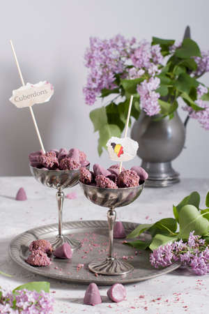 Belgian sweets cuberdon and pralines in silver glasses, spring still life with lilac flowers and flagsの写真素材