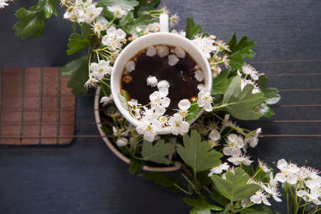 a cup of coffee with white flowers stands on the strings of a vintage black guitarの写真素材
