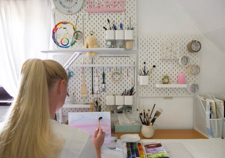 Back view of a blonde girl draws in a home studio equipped in modern design.の写真素材