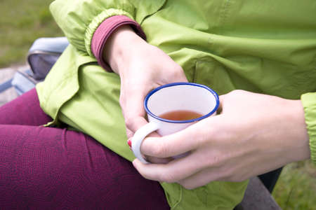 female hands holding an iron mug with tea during a pause in training, a tourist at a haltの写真素材