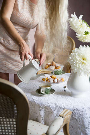 tea break in english style, vintage retro still life, homemade buns and a bouquet of white dalias,woman pouring a drink into a cupの写真素材