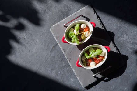 baked cherry tomatoes in portioned saucepans in the sunlight on the table, flat lay, copy spaceの写真素材