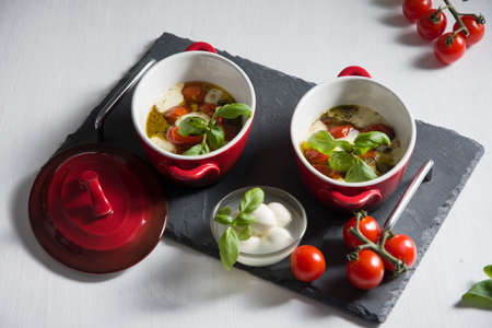 Italian caprese salad, baked cherry tomatoes, mozzarella and basil on a white table, still life