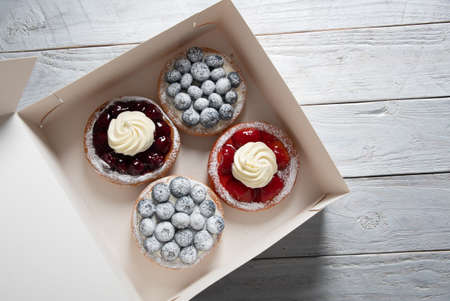 different pastries in a box, fresh cakes with berries and whipped cream,