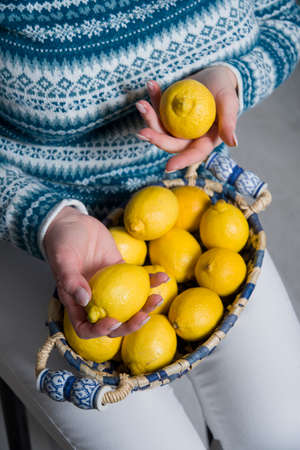 A woman in a blue sweater holds a basket with ripe yellow lemons in her handsの写真素材