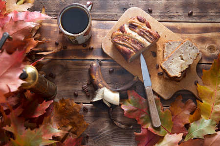banana cake on the wooden table with orange autumn leaves, copper coffee grinderの写真素材