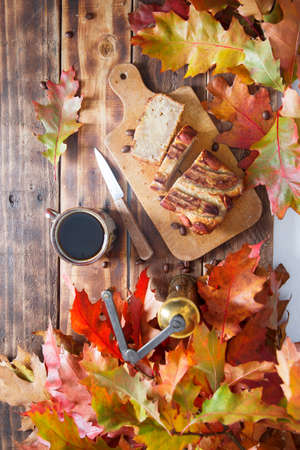 banana cake on the wooden table with orange autumn leaves, copper coffee grinder