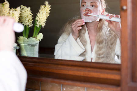 a woman in a mask brushing her teeth with an electric toothbrushの写真素材