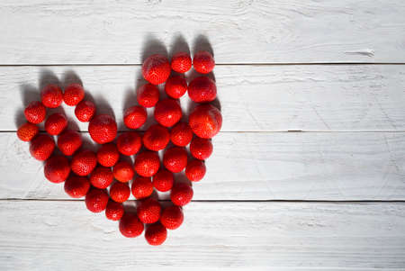 heart made from fresh strawberries on a wooden plank background