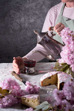 a woman pours tea from a silver teapot, background of pink sakura flowers,easter