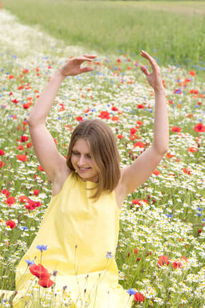 a beautiful young blonde woman in a yellow dress stands among a flowering fieldの写真素材