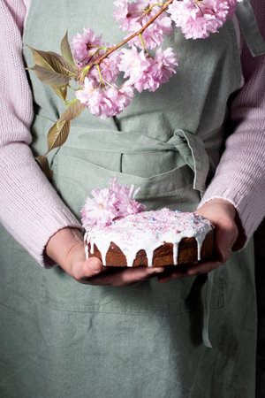 a woman decorates a homemade Easter cake with pink sakura flowers,spring blossom