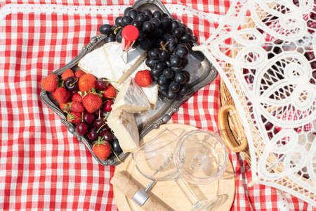summer picnic on a green lawn with red wine, cheese and fresh berries, grapes
