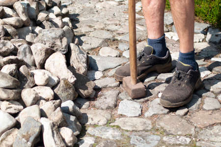 a gardener in dirty work clothes and boots holds a two-bladed iron hammerの写真素材