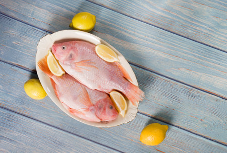 raw fresh pink tilapia fish lies on a platter surrounded by yellow lemons
