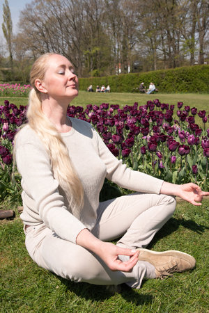Young beautiful woman in the park with spring tulips does yoga on the lawnの写真素材