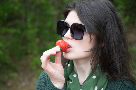 young beautiful brunette woman eat strawberry dessert at picnic on the benchの写真素材