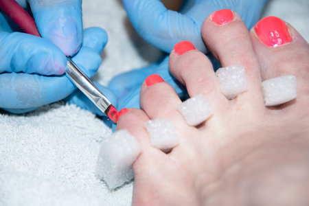 pedicure master paints clients toenails with orange gel polish, foot careの写真素材