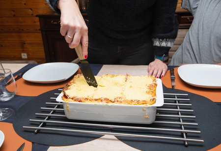 Woman cut with knife hot tasty home baking lasagna in ceramic casserole dishの写真素材