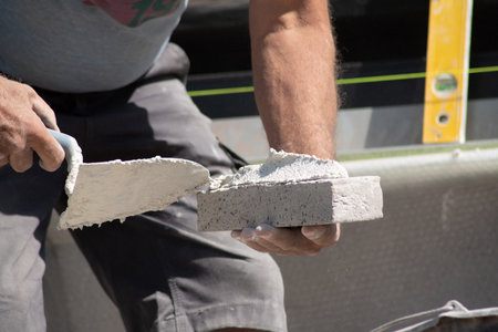 close up of the hands of a bricklayer applying cement mortar to a brickの写真素材