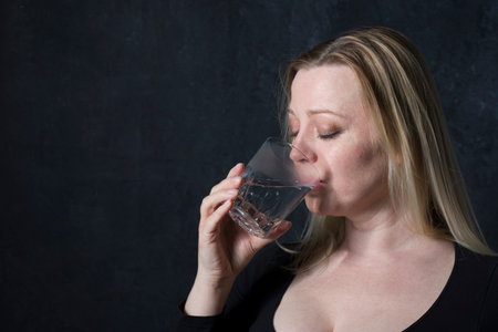 portrait caucasian middel aged woman in black blouse drinking water in the Dark room,healthy lifstile conceptの写真素材