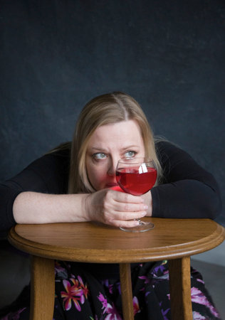 portrait of a depressed middle aged woman sitting alone at a table and holding glasses of red wine, burnoutの写真素材