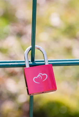 Pink metal lock on a fence in a park with an image of two hearts. Traditionally, people hang a padlock after a wedding to keep love in their hearts forever, Valentines Day, High Quality Photoの写真素材