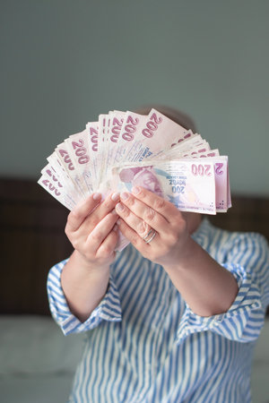 woman holds large stack of 200 Turkish lira bills in front of her, spreads it with a fan and shows...