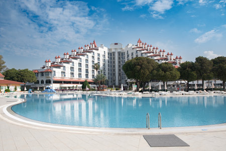 View of the main building of the Green Max Hotel, from the courtyard in front of the swimming pool with blue water and green palm trees, Belek, Turkey, May 29, 2024.のeditorial素材