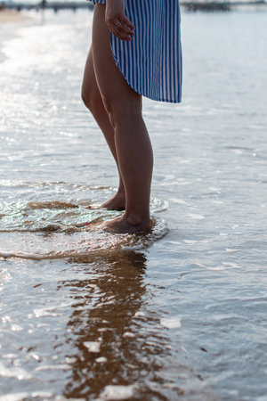 young woman barefoot walks along the sandy beach by the sea at sunset, plunging her feet into the...