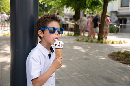 Cute child boy with a dirty face eats ice cream, the child enjoys dessert, walk in the park, High...