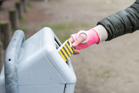woman with a pink cast on her arm throws garbage into a street trash can, ecology of a modern city, limited mobilityの写真素材