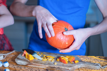 teenager in blue t-shirt picks pumpkin seeds out of pumpkin to create DIY halloween decor, traditional autumn holiday,の写真素材