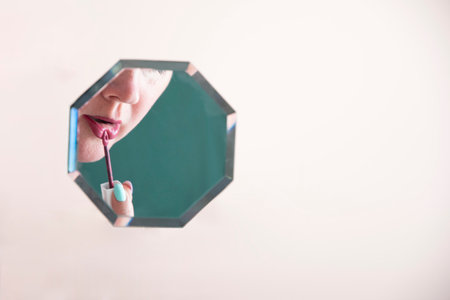 reflection of a woman in the mirror who paints her lips with lipstick, mirror hanging on peach fuzz background,の写真素材