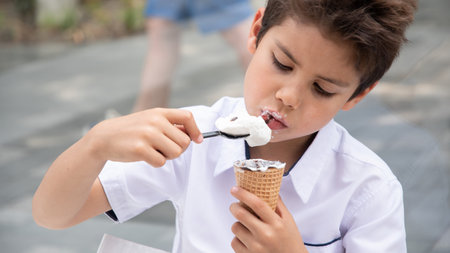 Boy happily eating ice cream on the street, his face covered in chocolate, refreshing dessert during a walk on a summer day, carefree peaceful childhood,の写真素材