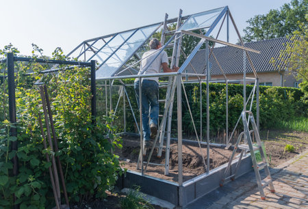 male gardener climbs ladder in greenhouse to roof strengthens structure does it with his own hands organic concept of growing vegetables in garden, DYI conceptの写真素材