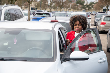 African American woman in a red coat opens the doors to get into a white car in a parking lot, personal transport, high quality photoの写真素材