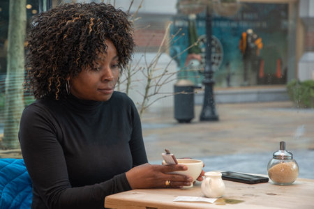 African young woman sits in a cafe in the morning, having just woken up, and drinks coffee, High quality photoの写真素材