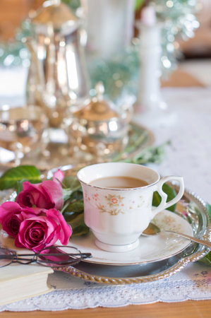 English style tea break, female hands pouring tea from a silver teapot into a porcelain cup, antique still life, antique tea set, shallow depth of field giving the scene a blur, light and air,の写真素材