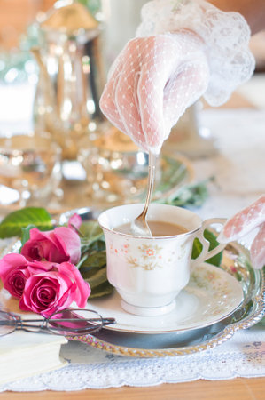 Tea break in English style, female hands in white lace gloves stirring cream in porcelain coffee cup, antique still life, silver tea set, shallow depth of field, light and air on Christmas morning,の写真素材
