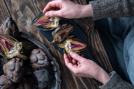 Woman cleaning fresh artichokes and cooking on wooden table, rustic still life top view,concept of healthy eating and fine dining,の写真素材