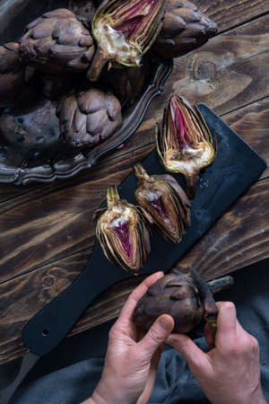 Woman cleaning fresh artichokes and cooking on wooden table, rustic still life top view,concept of healthy eating and fine dining,の写真素材