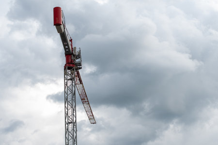 Tower crane with red trim against cloudy sky before thunderstorm captured in realistic photo, urban construction and infrastructure development concept, copy space,の写真素材