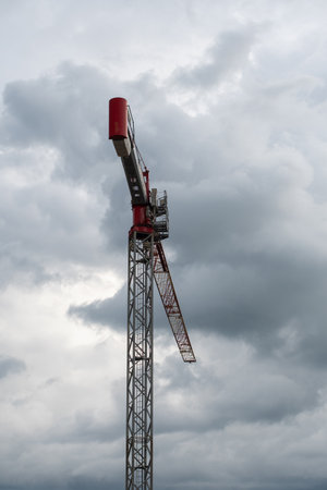 Tower crane with red trim against cloudy sky before thunderstorm captured in realistic photo, urban construction and infrastructure development concept, copy space,の写真素材