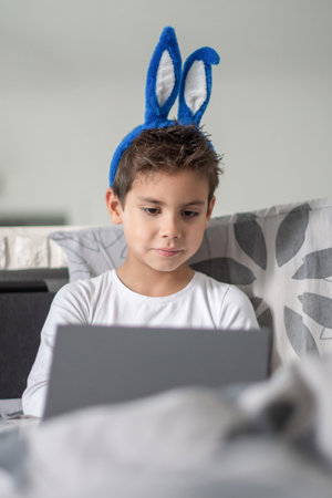 Boy with blue bunny ears sitting on sofa, concentrating on working on laptop, Casual atmosphere, playful and cheerful mood before Easter,の写真素材